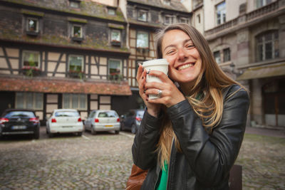 Portrait of cheerful woman having coffee while standing in city