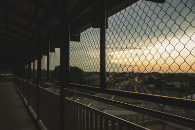 Chainlink fence on bridge against sky during sunset