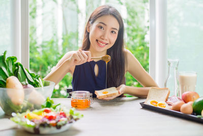 Portrait of young woman putting honey on bread