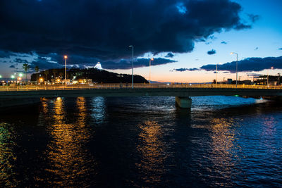 Illuminated bridge over river against sky in city at night