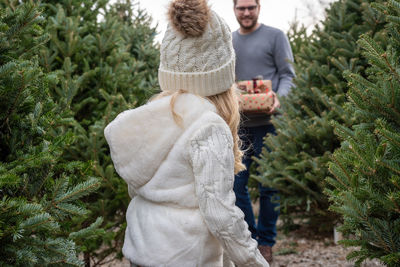 Father holding gifts walking towards daughter amidst christmas trees