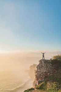 Scenic view of woman on rock against sky during sunset