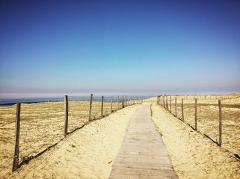 View of wooden walkway against clear blue sky