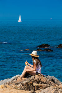 Rear view of woman sitting on rock by sea against sky