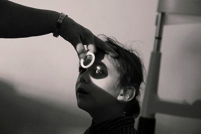 Cropped hand of male ophthalmologist examining boy against wall