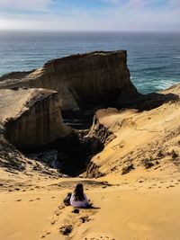 Rear view of people on rock at beach against sky