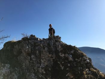Man standing on rock formation against clear blue sky