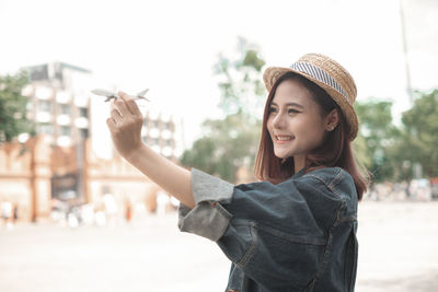 Portrait of smiling young woman standing against city in background