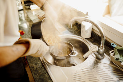 Young man pouring boiling water from saucepan on pasta in colander