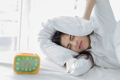 Alarm clock with young woman lying on bed at home