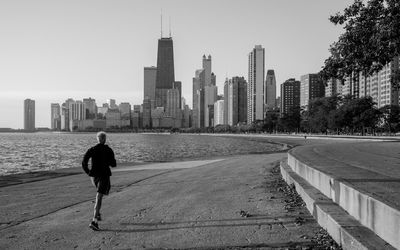Rear view of man walking on footpath against cityscape