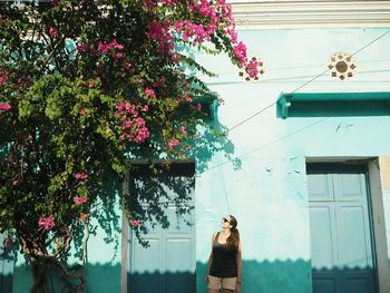 Woman standing by flowering tree against building