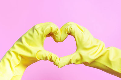 Close-up of hand holding heart shape against pink background