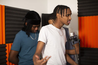 Teenage rapper with friends recording song on microphone in studio