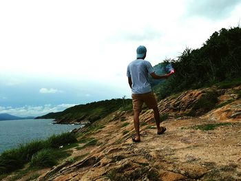 Rear view of man holding distress flare while standing on mountain against cloudy sky