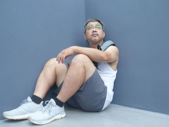 Mature man sitting on floor against blue wall