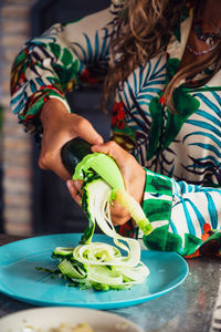 Female cutting fresh green cucumber while cooking salad in light kitchen