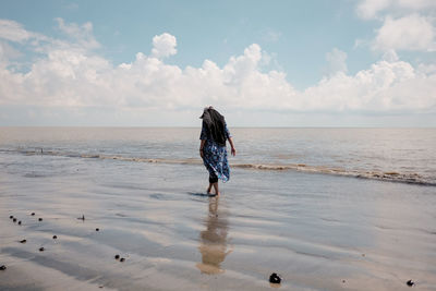 Rear view of woman standing at beach against sky