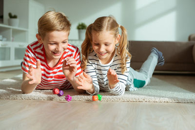 Cheerful siblings playing with dice while lying on carpet at home