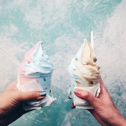 Cropped hands of women holding ice creams against wall