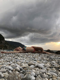 Woman lying on rock against sky