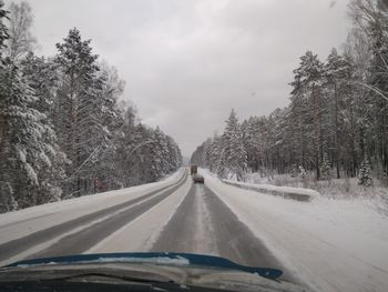 Road amidst trees against sky seen through car windshield during winter