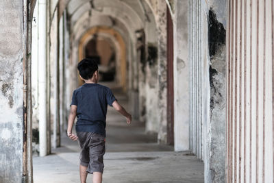 Rear view of boy walking in old corridor