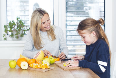 Mother and daughter cutting fruits on table at home