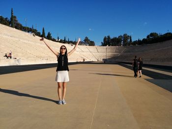 Full length of young woman with arms raised at panathinaiko stadium during sunny day