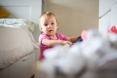 Mischievous baby plays with clothes in drawers, tidies up the bedroom