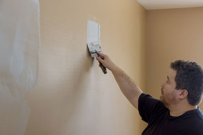 Portrait of man with arms raised against wall at home