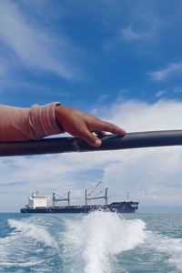 Person hand by sea against sky