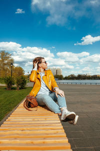 Young woman stylishly dressed in white sneakers, jeans sitting on street near pond. travel lifestyle