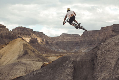 Rear view of young male jumping with mountain bike in desert landscape