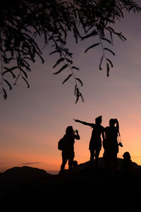 Low angle view of silhouette people standing on rock against sky