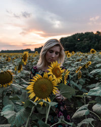 Portrait of woman with sunflower against sky during sunset