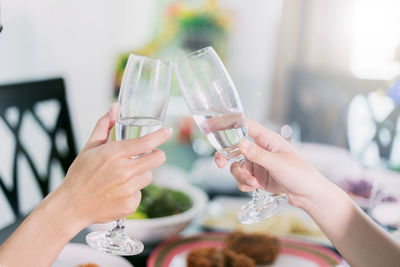 Cropped hands of female friends toasting champagne flutes at dining table