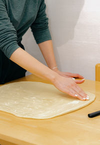 One caucasian young girl greases the dough on the table with butter.