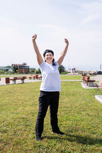 Full length portrait of smiling young woman standing on field