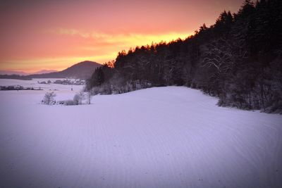 Snow covered landscape against sky during sunset