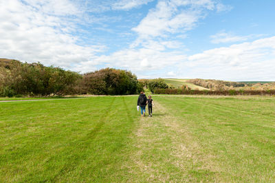 Rear view of men walking on field against sky