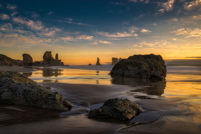 Rock formations at beach against sky during sunset