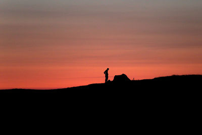 Silhouette person standing on land against sky during sunset