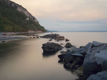 Scenic view of stones next to sea against cloudy sky