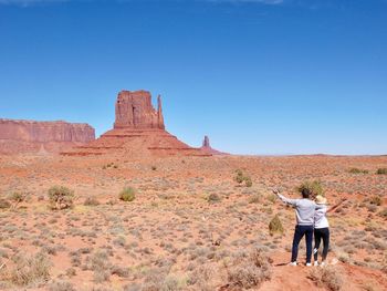Rear view of couple standing on land against rock formations and clear blue sky
