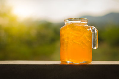 Close-up of orange juice in glass jar on railing