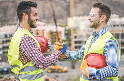 Side view of smiling engineers holding hands at construction site