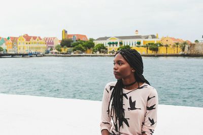 Young woman on retaining wall by sea against sky