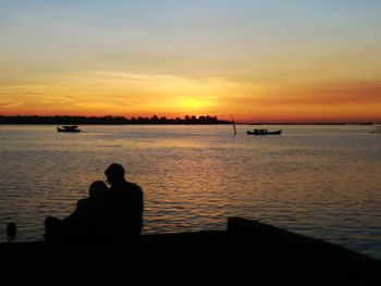 Silhouette people looking at sea against sky during sunset