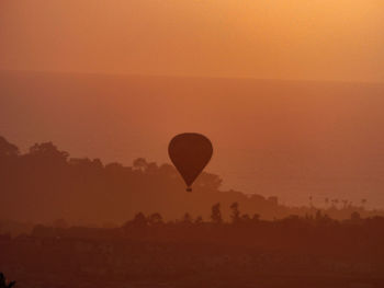 Silhouette of hot air balloon flying against orange sky